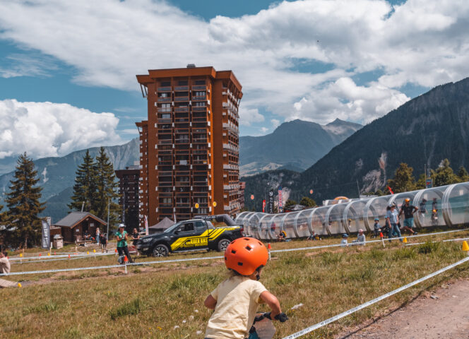 Photo d'un enfant qui fait du vélo devant le tapis de remontées et un immeuble du Corbier